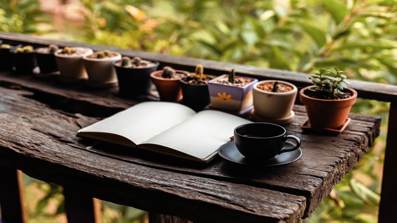 Open notebook with handwritten notes beside a cup of coffee on a greenhouse potting bench